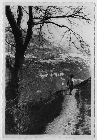 Donna su un sentiero montano, sullo sfondo i prati di Arla