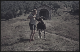 Ragazzo con capra davanti alla cappella sui monti di Cimadera